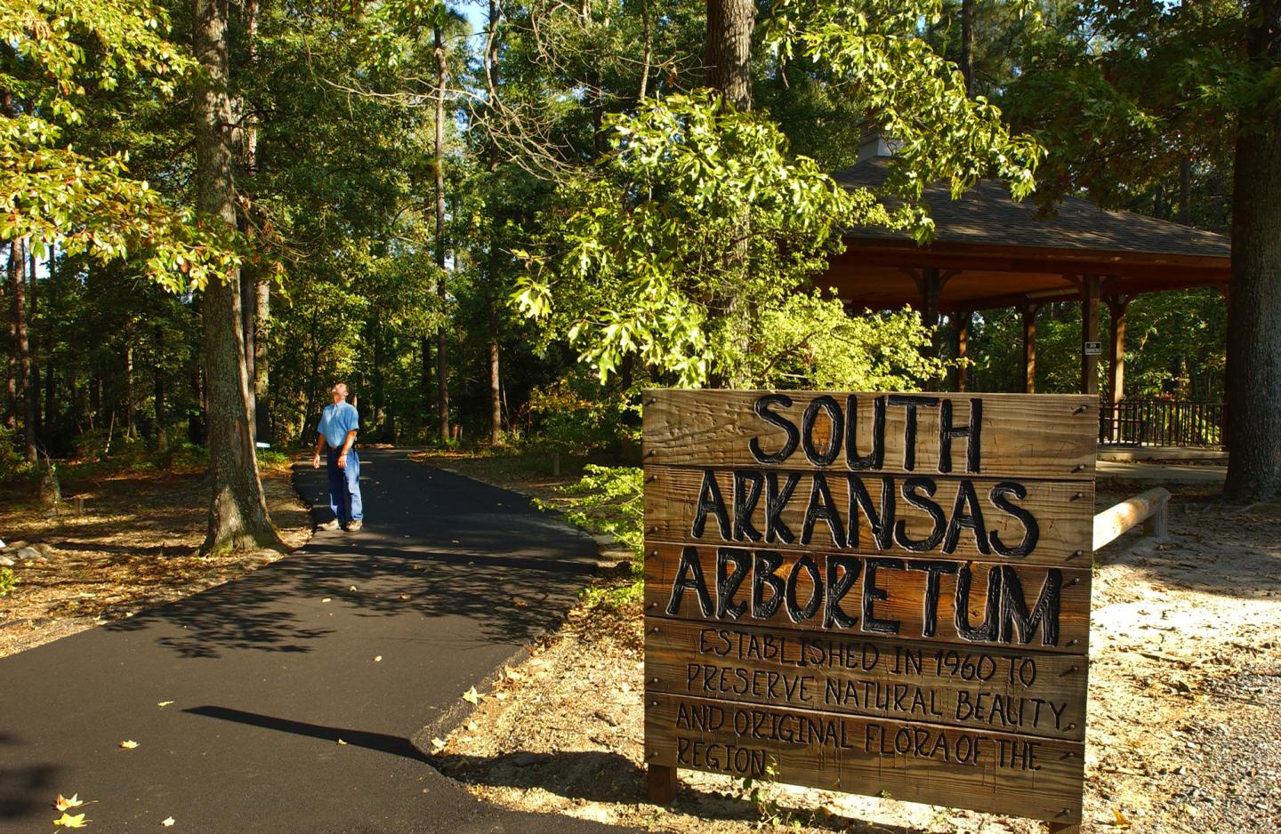 Path through a forest with a wooden sign for South Arkansas Arboretum.