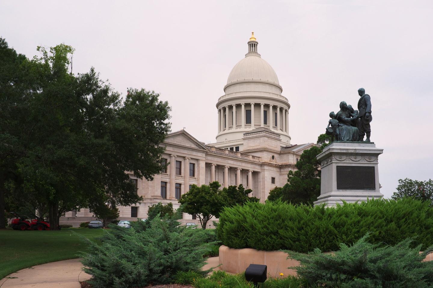 Capitol building with dome, surrounded by trees and a statue in the foreground.