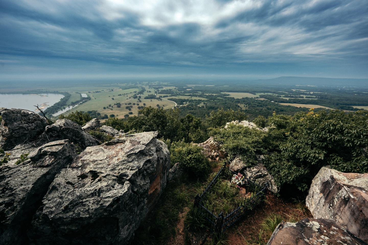 Rocky hilltop overlooking lush green fields under a cloudy sky.