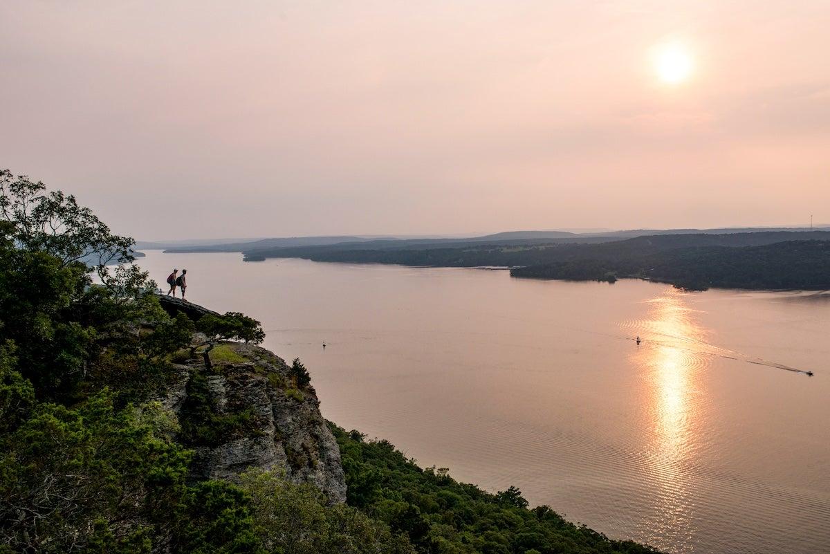 Sunset view over a calm lake with distant cliffs and trees.