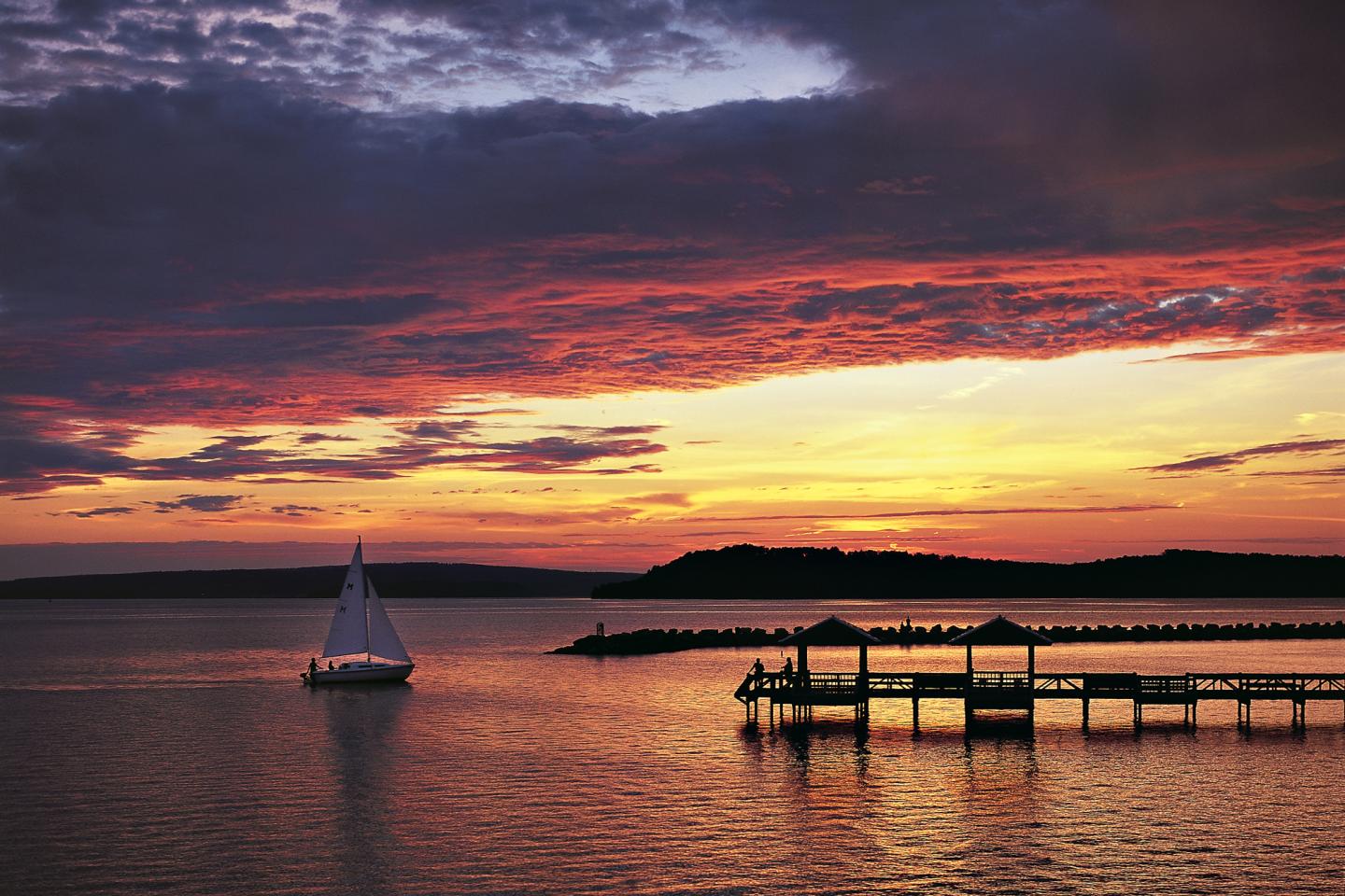 Sailboat on calm water at sunset with vivid orange and purple sky.