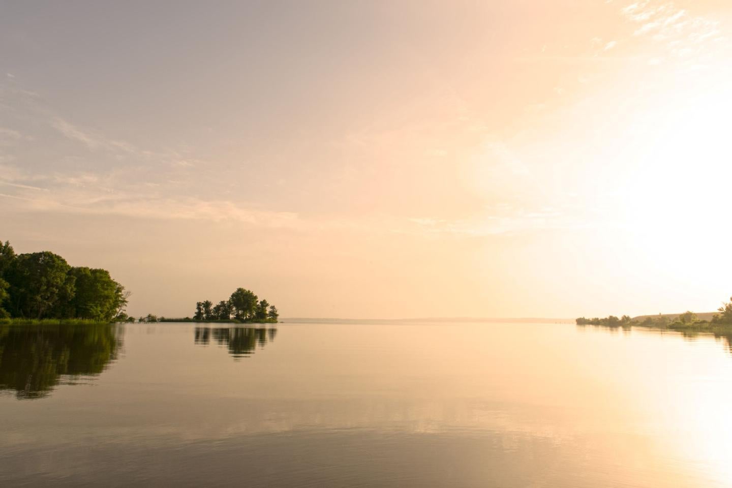 Tranquil lake at sunrise with a tree-lined shore and calm waters.