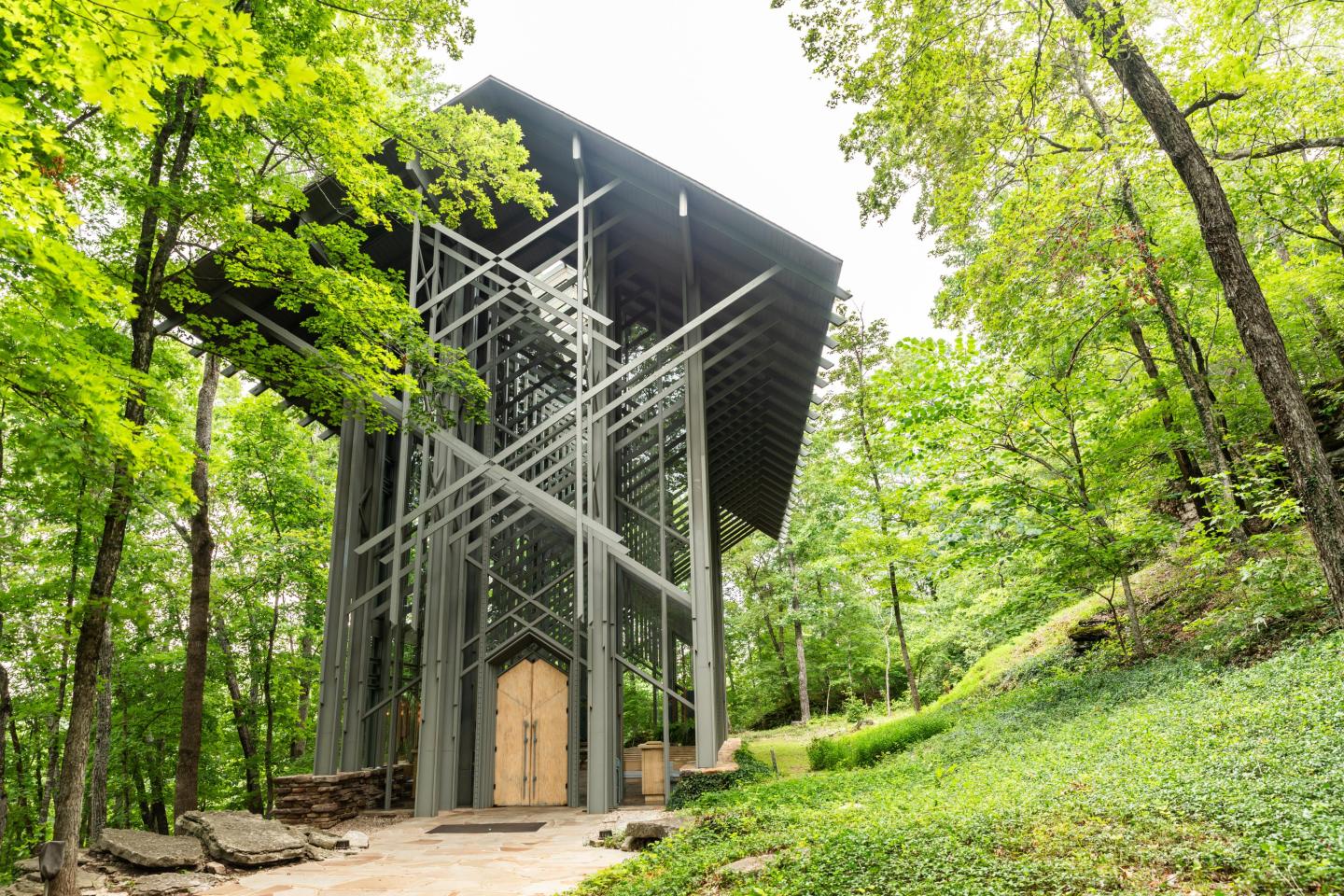 Wooden chapel in a forest, surrounded by tall green trees.