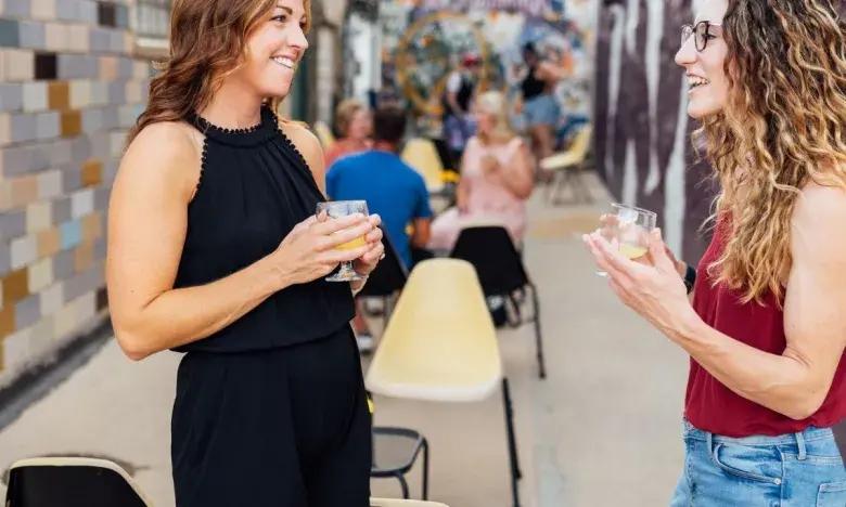 Two women smiling and chatting outdoors, holding drinks.