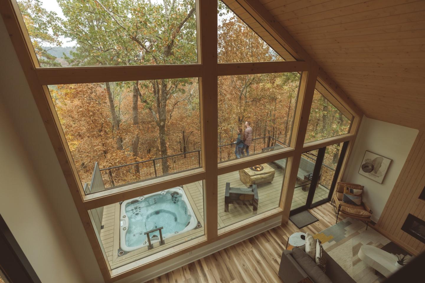 Large windows overlook a deck with a hot tub and autumn trees.