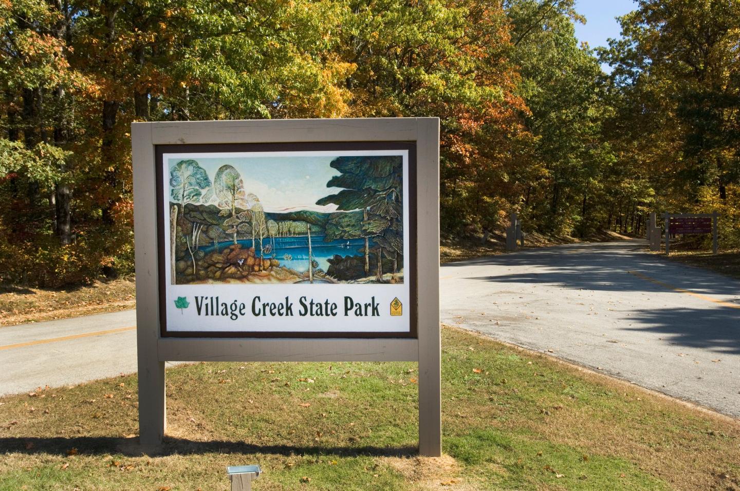 Sign for Village Creek State Park by a road, surrounded by autumn trees.