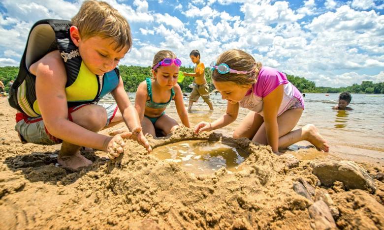 Kids playing on a sandy beach by the water under a bright sky.