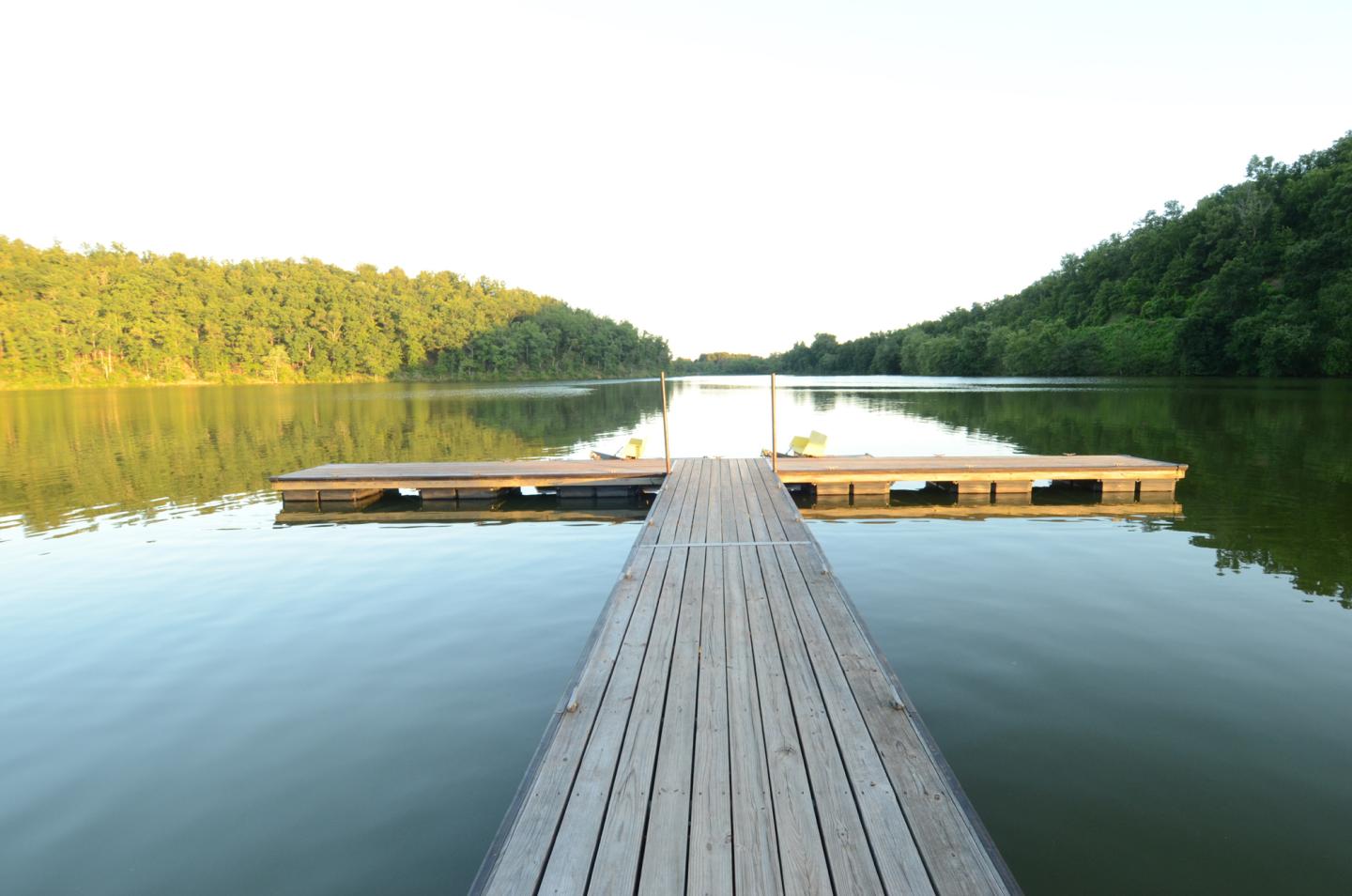 Wooden dock extending into a calm lake, surrounded by lush green trees.