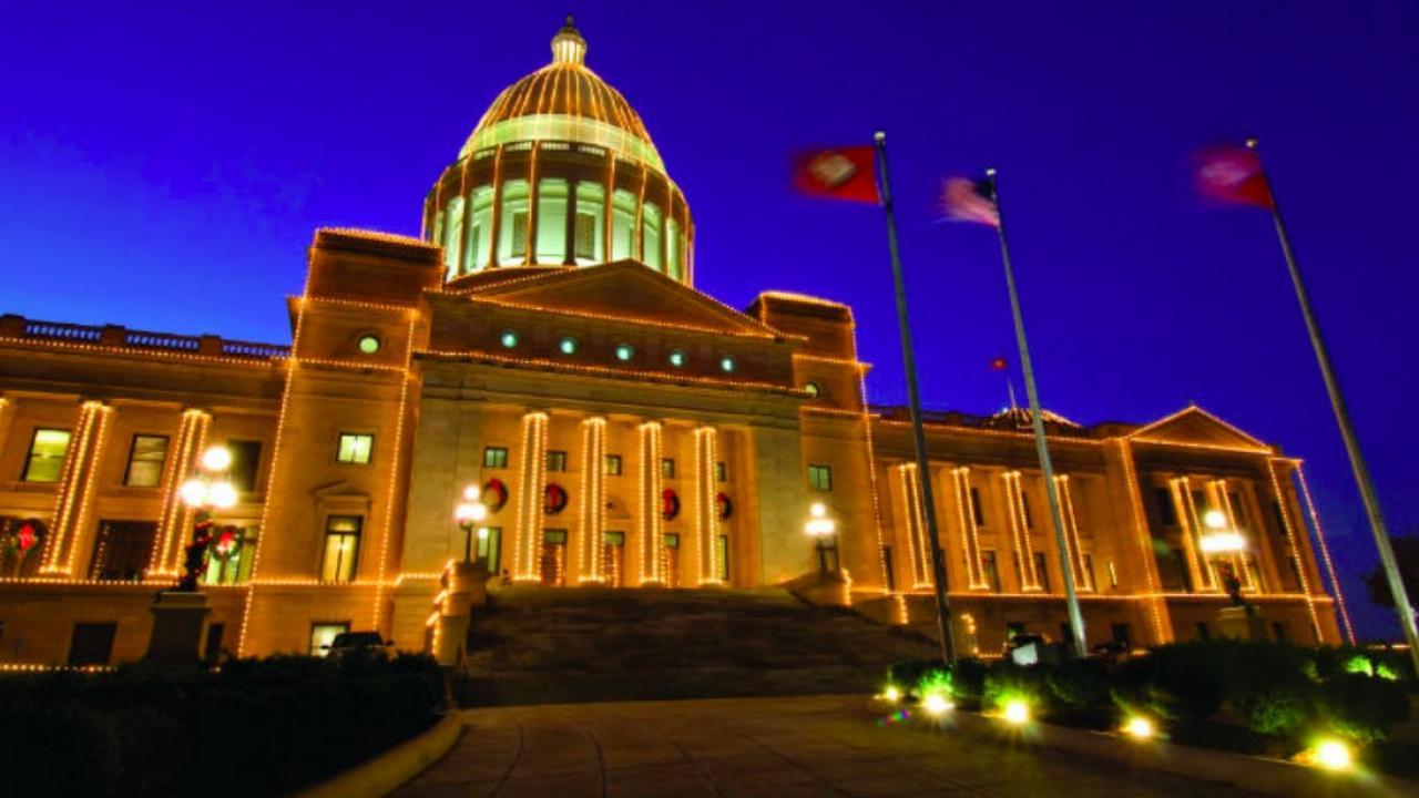 Capitol building at night, warmly lit with flags and a deep blue sky.