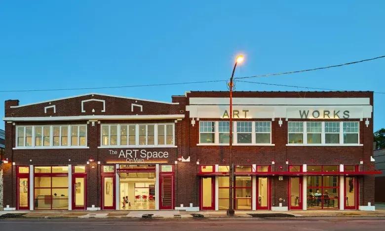 Brick art studio buildings at dusk with lit windows and a streetlamp.