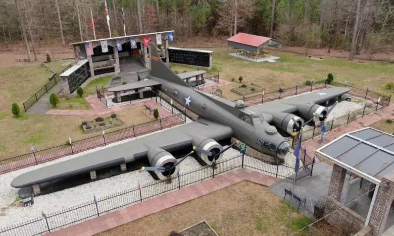 Aerial view of a B-17 bomber at a memorial site, surrounded by trees and flags.