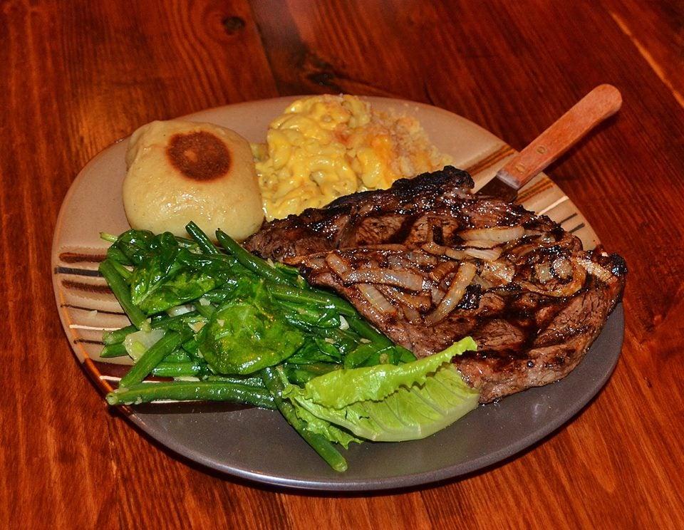 Grilled steak with onions, mashed potatoes, greens, and a roll on a plate.