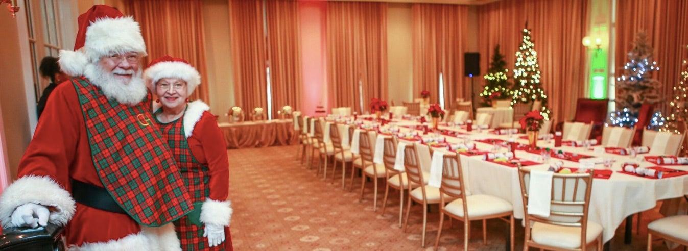 Santa and Mrs. Claus smiling in a festive, decorated banquet hall.
