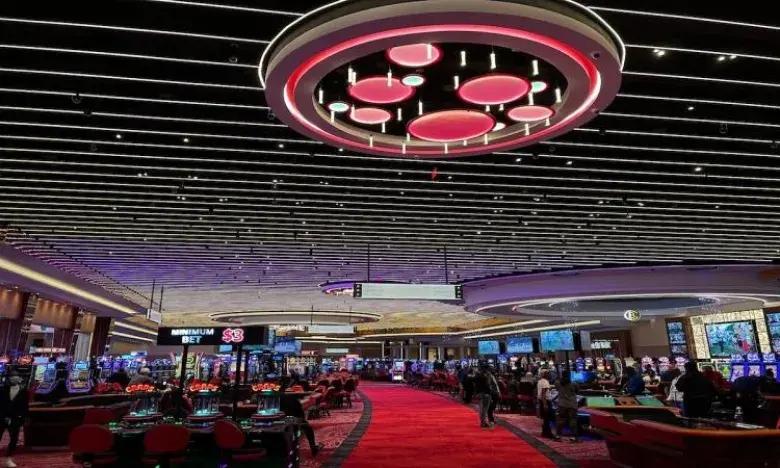 Casino interior with gaming tables, red carpet, and bright ceiling lights.