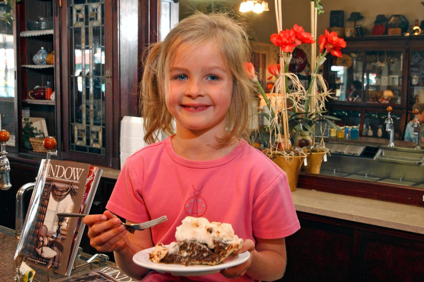Young girl smiling with cake in a cozy café setting.
