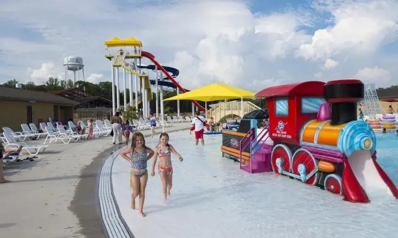 Children playing near colorful slides and inflatable train in a water park.