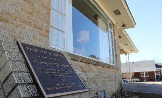 Plaque on brick wall near house window reflecting a lamp, sunny day.
