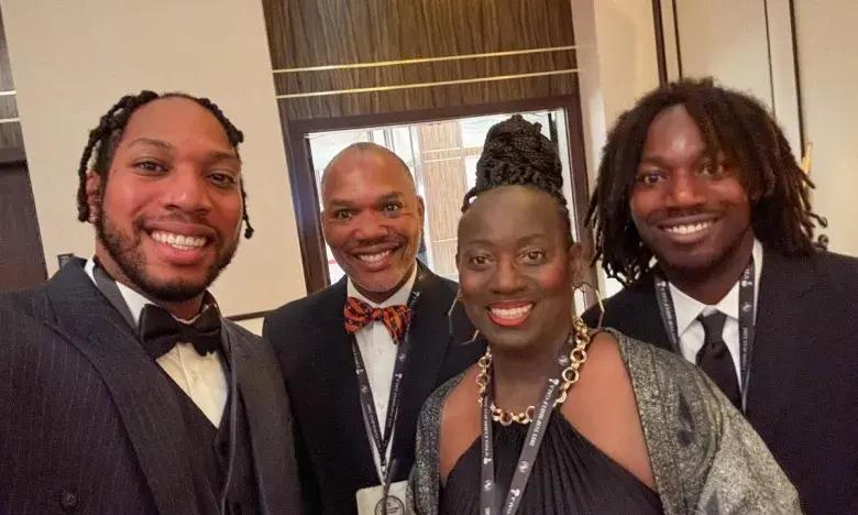Four people smiling in formal attire at an indoor event.