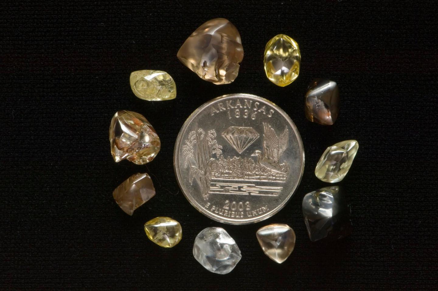 Round gray coin surrounded by various colored gemstones on black background.