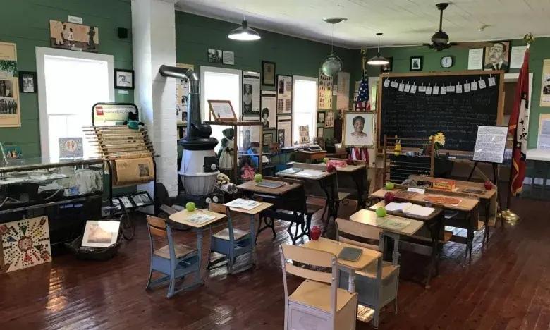 Old-fashioned classroom with wooden desks, green walls, and artwork.