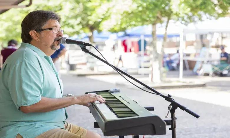 Man playing keyboard and singing outdoors at a park.