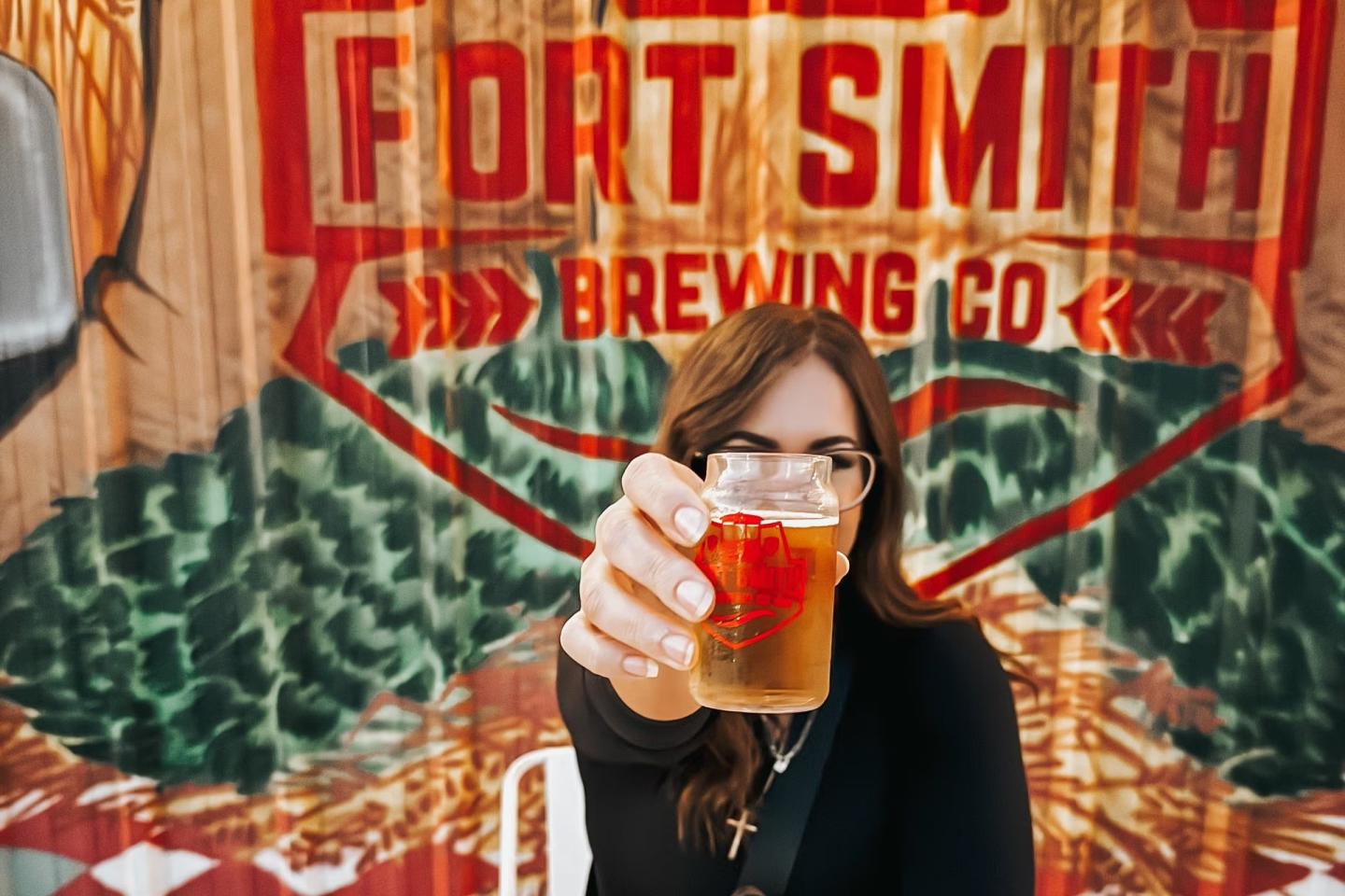 Woman holding a beer glass at Fort Smith Brewing Co sign.