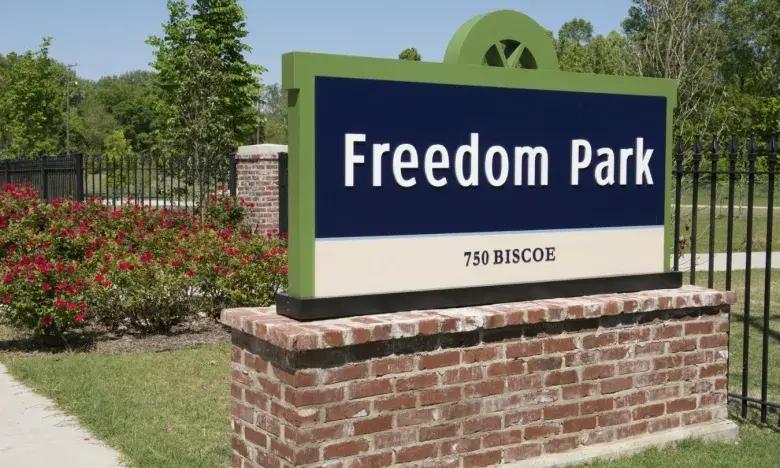 Freedom Park sign on a brick base, surrounded by greenery and flowers.