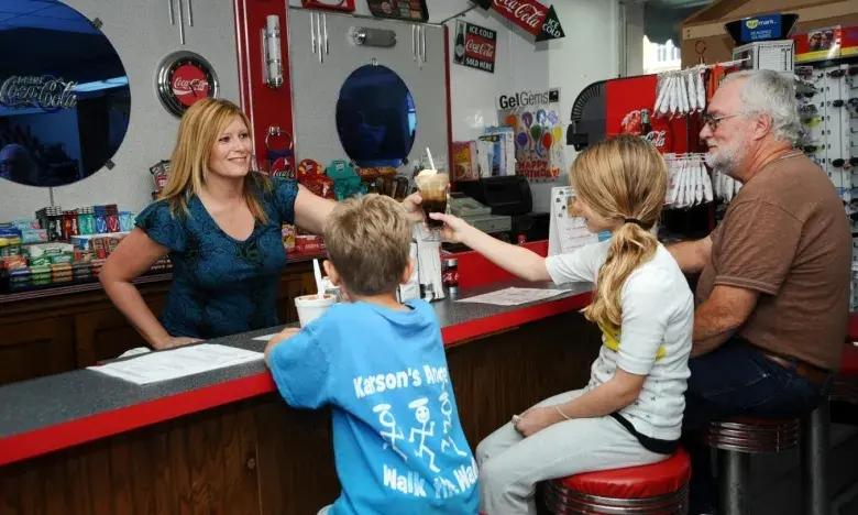 Server handing ice cream to patrons at a retro diner counter.