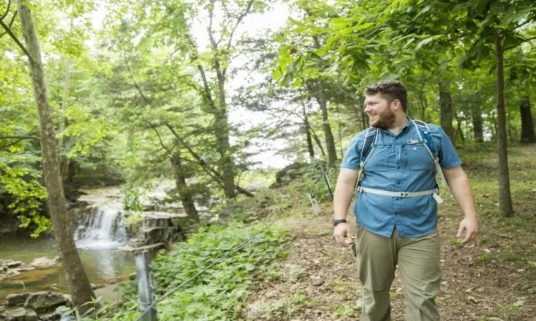 Man hiking near a forest waterfall, looking right.