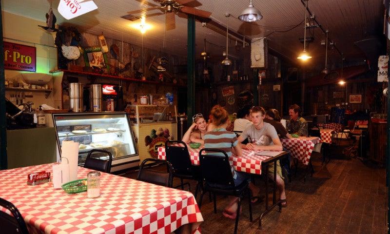 Cozy rustic diner with red checkered tablecloths and ceiling fans. People dining.