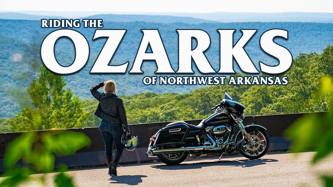 Motorcyclist overlooks lush, green Ozark landscape under a clear blue sky.