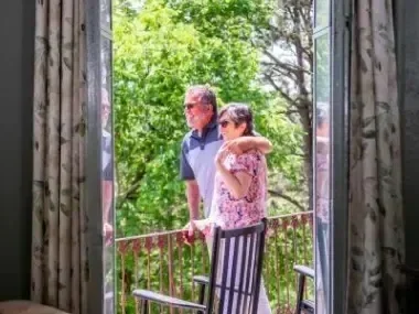 Couple standing on a balcony, looking at lush green trees.