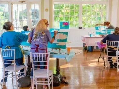 People painting on canvases in a sunlit room.
