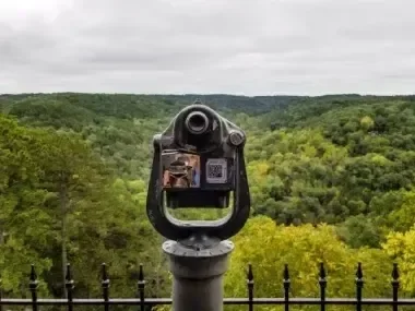 Coin-operated binoculars overlooking a lush green valley.