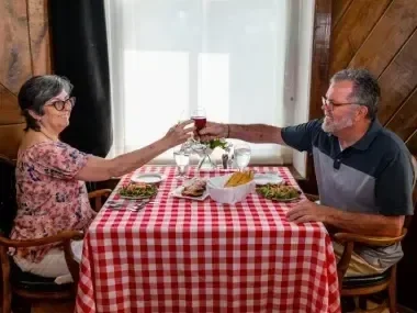 Elderly couple toasting at a table with a red checkered tablecloth.