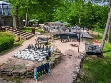 Outdoor chess set on stone path with seating, surrounded by lush greenery.