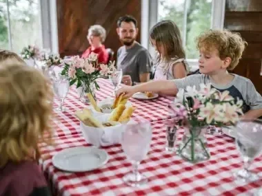 Family dining at a table with a red checkered tablecloth and flowers.