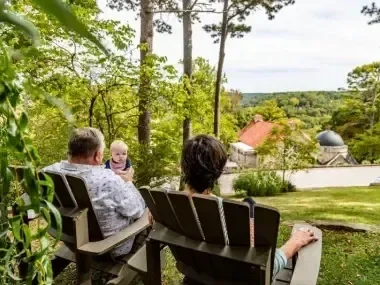 Family seated in Adirondack chairs, enjoying a scenic, wooded view.