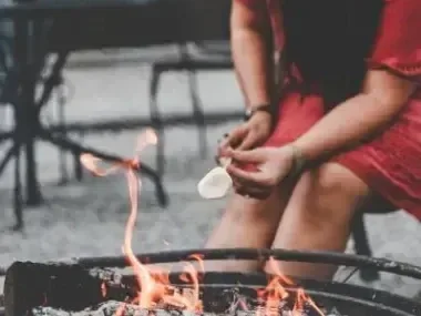 Person roasting marshmallow over outdoor fire pit.