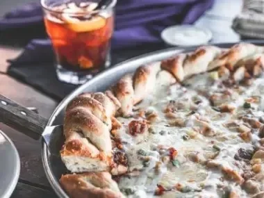 Cheesy pizza on a tray with a drink and purple cloth nearby.