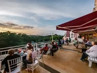 A terrace with people dining at sunset under a red canopy.