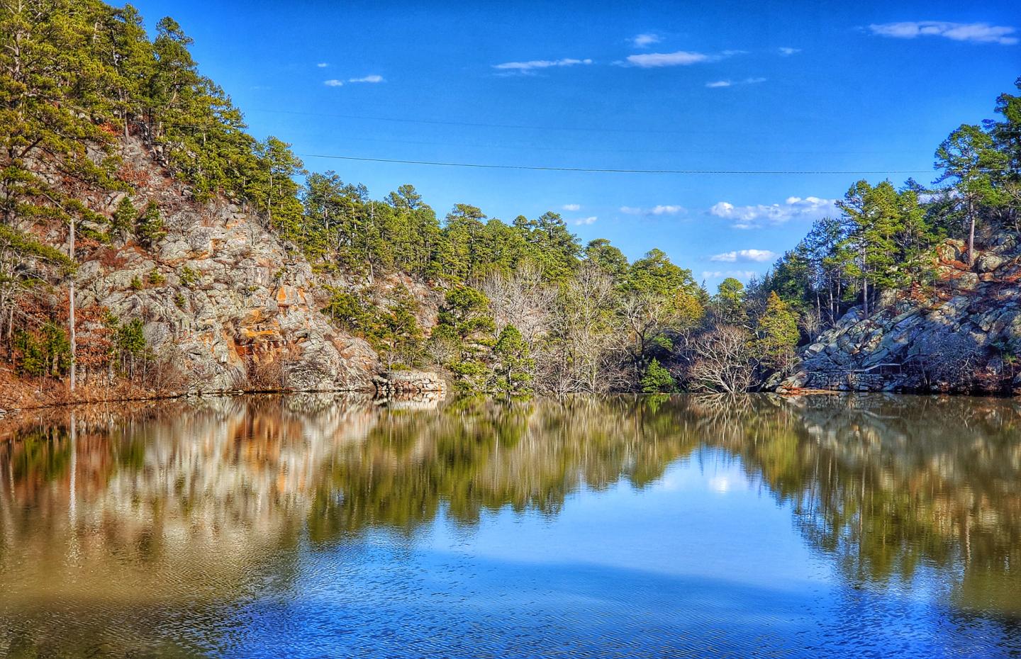 Calm lake reflecting trees and blue sky with clouds.