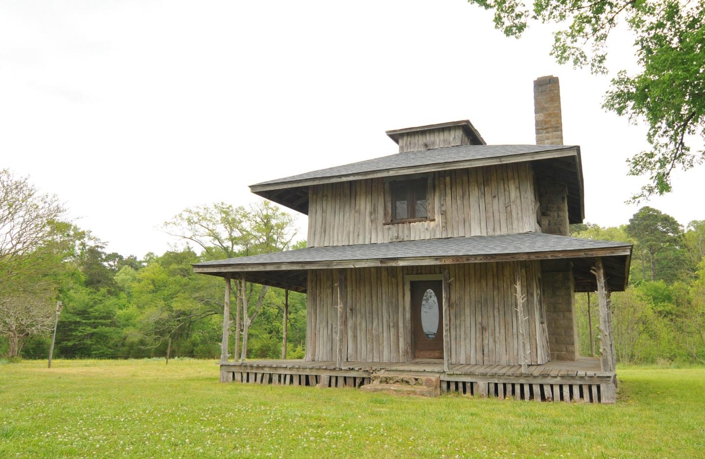 Old wooden house in a green field under a cloudy sky.