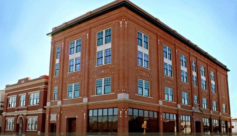 Red brick, four-story building with many windows under a clear blue sky.