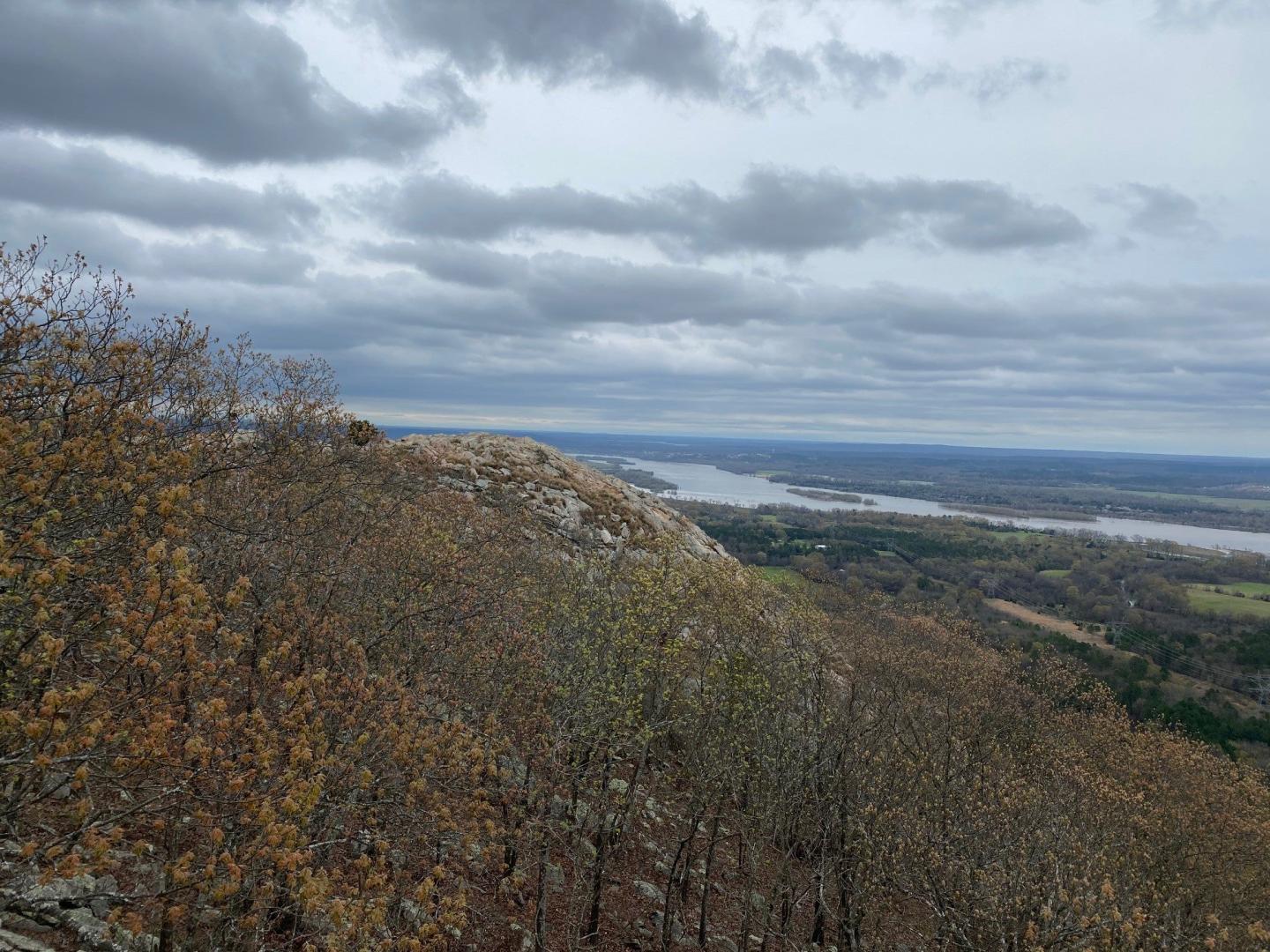 Overcast sky above a rocky hill with autumn trees and distant river.