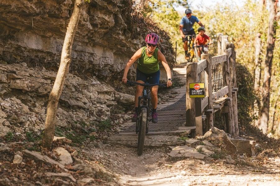 Cyclists on a rocky trail, trees in the background, one cyclist leading the group.