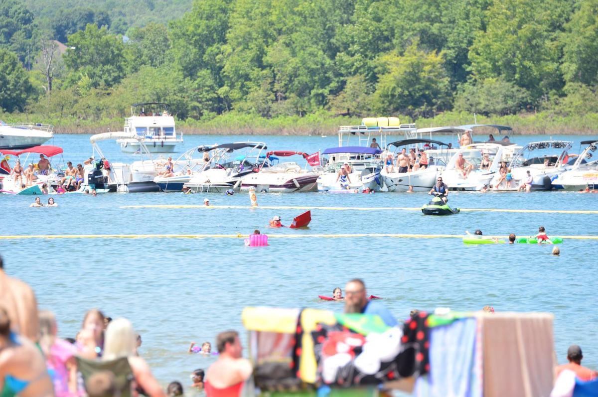 Crowded lake scene with boats, swimmers, and sunbathers.