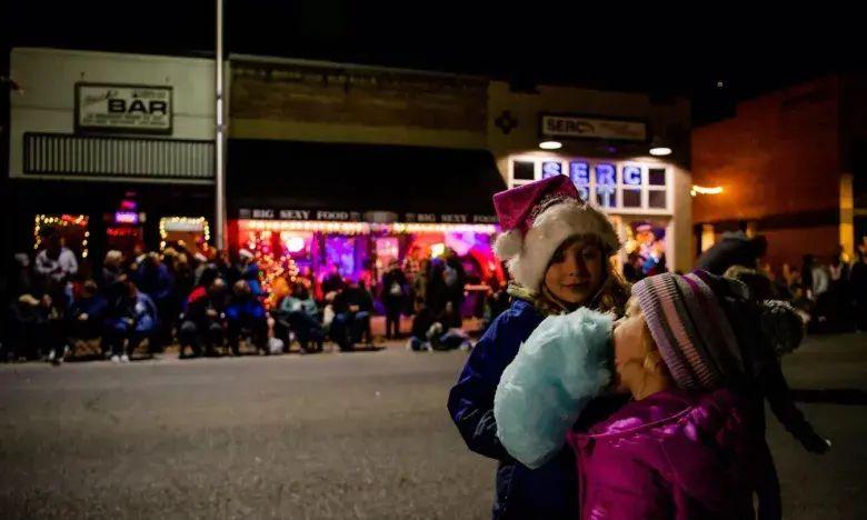 Two children in winter attire hug on a dimly lit street during a nighttime event.
