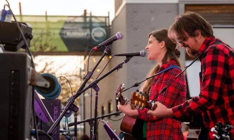 Musicians in plaid shirts performing outdoors with guitars.