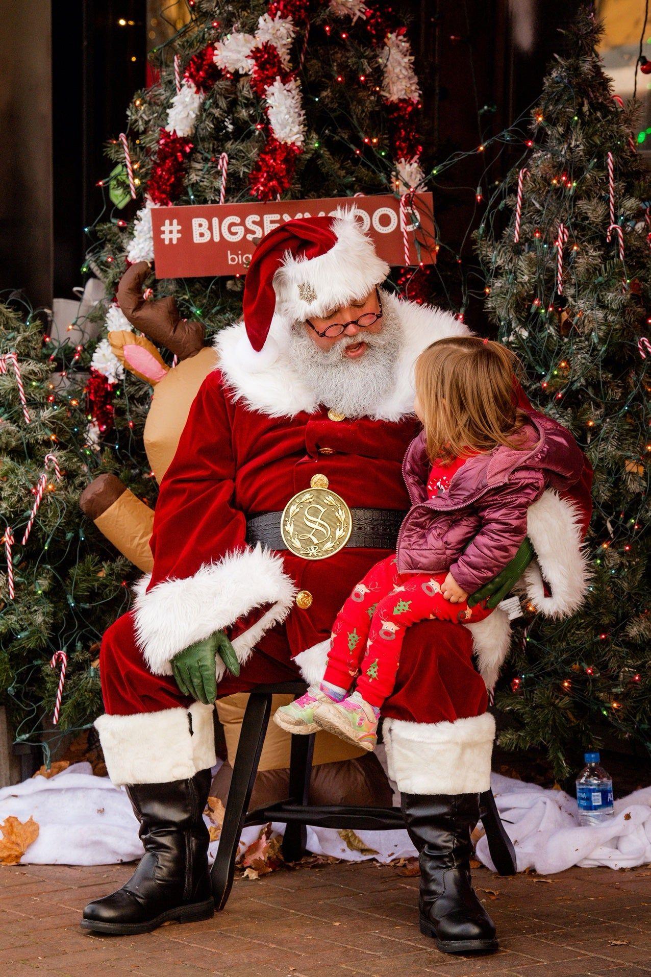 Santa with a child on his lap, surrounded by decorated Christmas trees.
